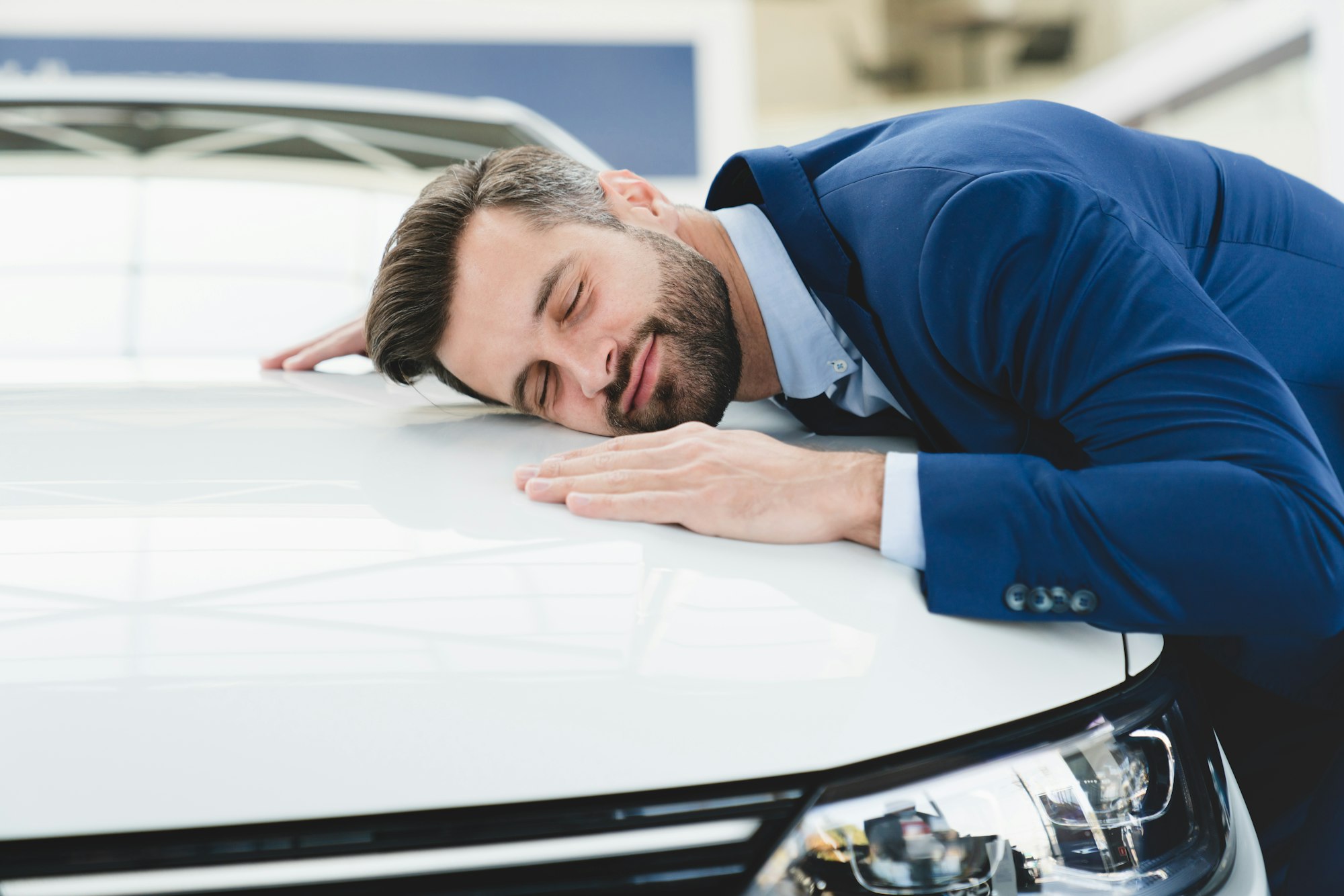 Businessman hugging car, feeling excited after buying expensive auto at auto dealer shop store.